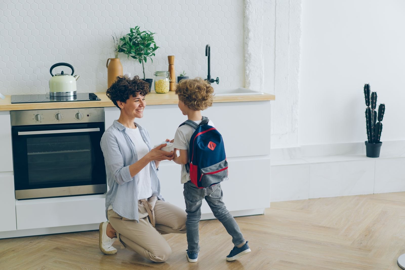 Smiling mother and son with backpack in kitchen