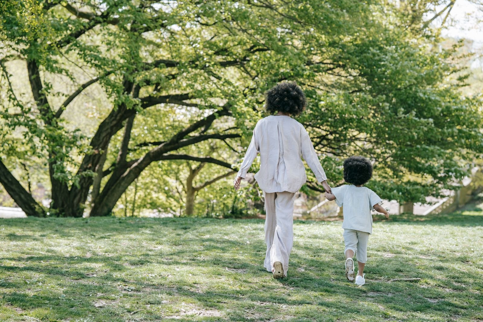 A woman and her child holding hands while walking at a park